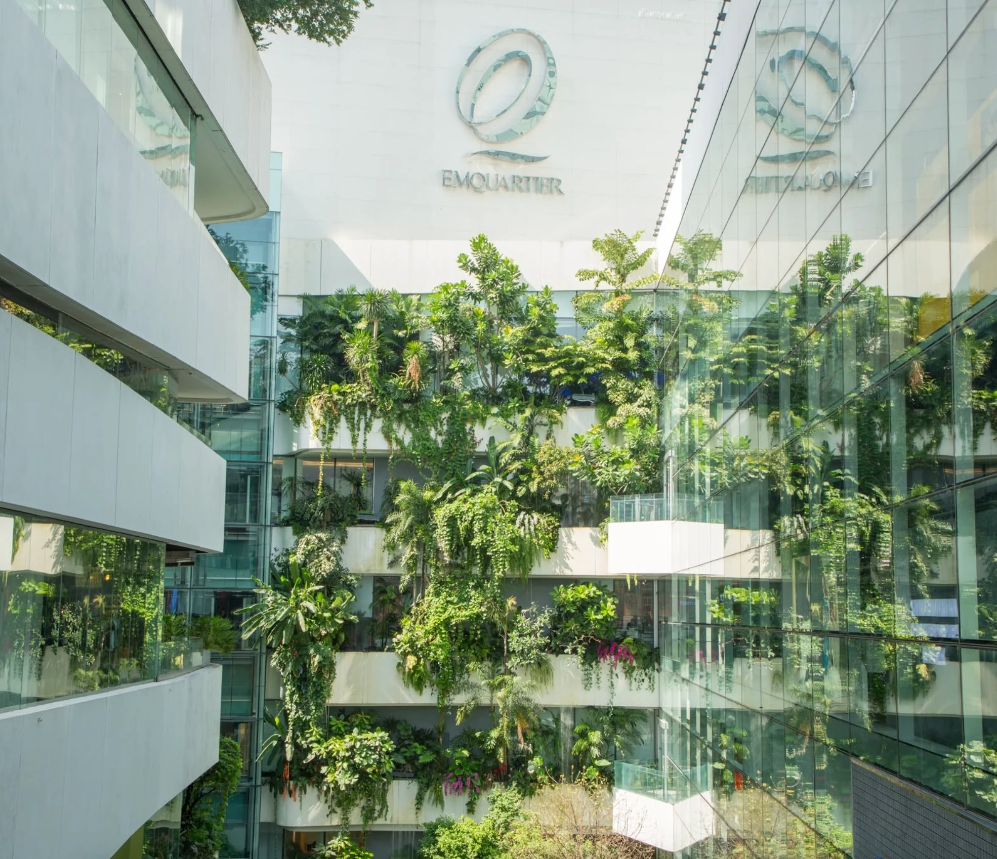 Layered tropical planting, pale stone balconies, and glass reflections at EmQuartier